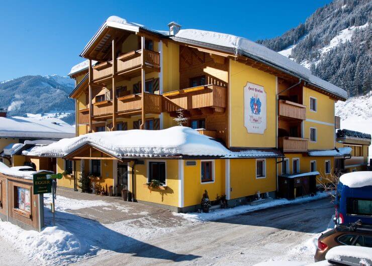 Schneebedecktes Hotel Egger - gelbe Fassade mit Holzbalkonen