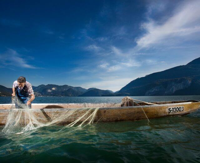 Fischer auf Boot im See – Via Culinaria Hauptsujet Mann mit Fischerboot und Fischernetz im See.