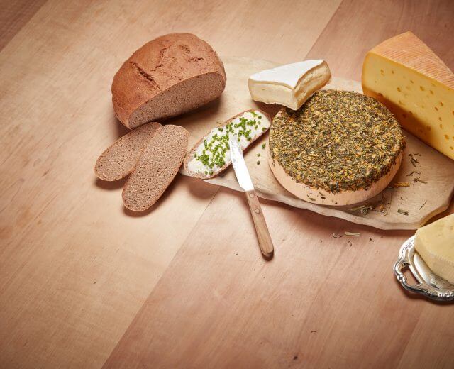 Verschiedene Käsesorten und Bauernbrot liegen neben einem Schnittlauchbrot mit Butter