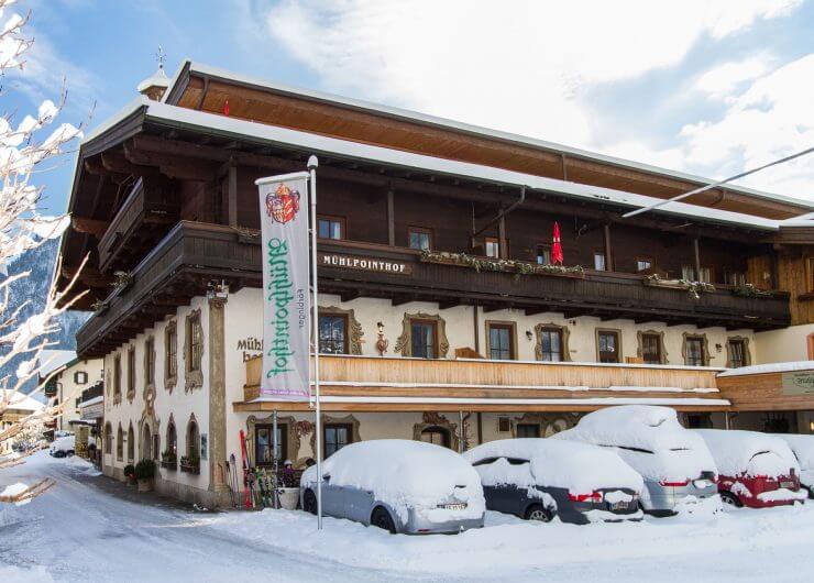 Winterlicher Mühlpointhof mit verschneiten Autos am Parkplatz