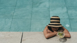 Eine Person mit gestreiftem Hut entspannt sich mit einem Getränk in der Hand am Pool des Bioparadieses im Hotel SalzburgerLand.