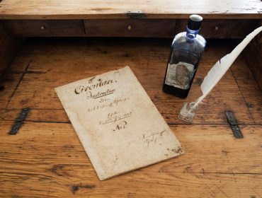 Schulzirkular – Arnsdorf Altes handgeschriebenes Dokument, Tintenfass und Federkiel auf einem rustikalen Holztisch.