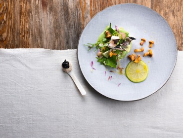 Werfener Forelle mit Sizilianischer Zitrone und Kaviar von Walter Grüll Eine Haubenküche mit Gemüse, Pilzen und essbaren Blüten auf einem grauen Teller mit Kaviar.
