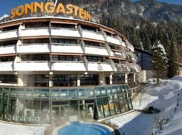 Verschneites Hotel Sonngastein mit Glaseingang und Außenpool, eingebettet in eine winterliche Berglandschaft.