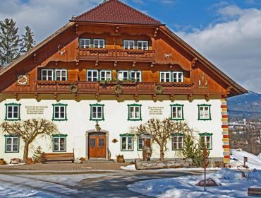 Ein traditionelles Alpenhaus auf dem Bio-Bauernhof Suppangut mit Holzbalkonen und verschneitem Bergblick.