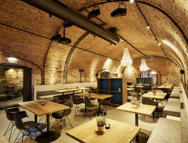 Modernes Restaurant mit gewölbter Ziegeldecke, Holztischen, Kronleuchtern und minimalistischem Dekor.