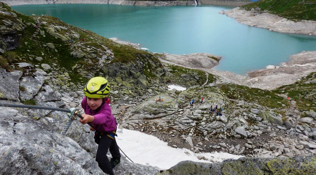 Kind klettert in der Wand, im Hintergrund ist der Weißsee sichtbar