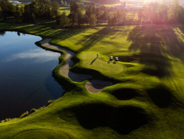 Luftaufnahme eines Golfplatzes mit Sandfängen, grünem Gras und einem Teich bei Sonnenuntergang.
