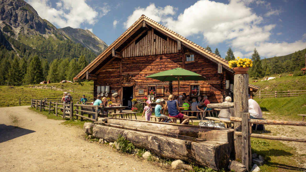 Die Menschen genießen die Almsommer-Eröffnung vor der rustikalen Tauernkarleitenalm in den Bergen, umgeben von Natur und Bäumen. (vergrößerte Ansicht)