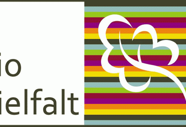 Bio Vielfalt Text mit weißem Blumenumriss auf bunt gestreiftem Hintergrund.