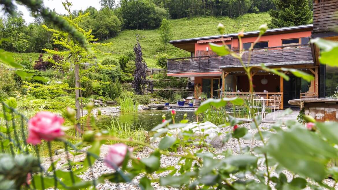 Haus mit Schwimmteich umgeben von einem blühenden Rosengarten, Wiese und Wald