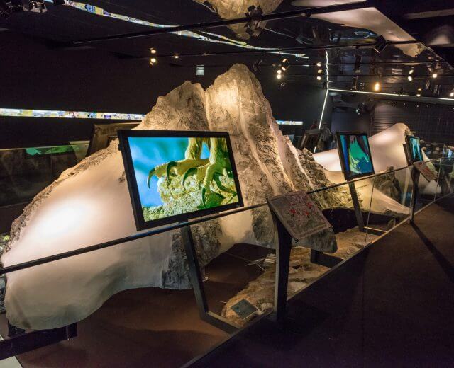 Genussreisen im SalzburgerLand, Nationalpark Hohe Tauern Großglockner Hochalpenstraße Ausstellung mit großen, weißen Felsformationen und Bildschirmen, die Vögel in einem schwach beleuchteten Museum zeigen.
