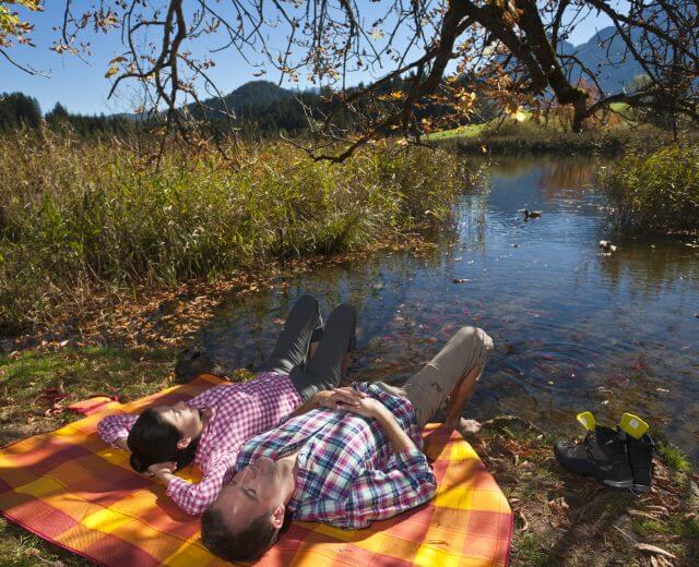 AGS, Gesundheit, Tennengau, Entspannung am See Pärchenliegt auf einer orange-karierten Picknickdecke am Seeufer unter einem Baum