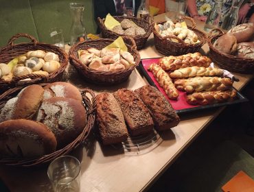 Verschiedene Brote und Brötchen in Körben auf einem Tisch, darunter geflochtenes Brot und Körnerbrote.