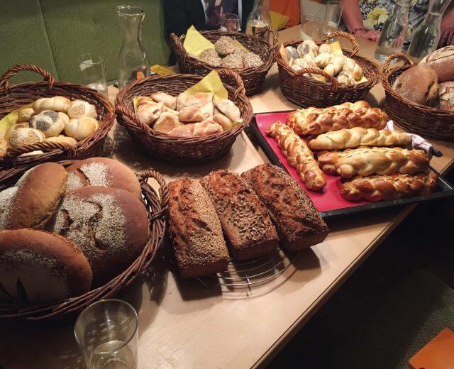©„backenmitchristina“_Bramlhof Verschiedene Brote und Brötchen in Körben auf einem Tisch, darunter geflochtenes Brot und Körnerbrote.