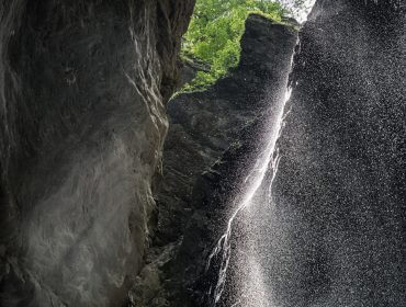 Das Sonnenlicht scheint durch den Nebel des Liechtensteinklamm-Wasserfalls, der sich zwischen hohen, grünen Felsen befindet.