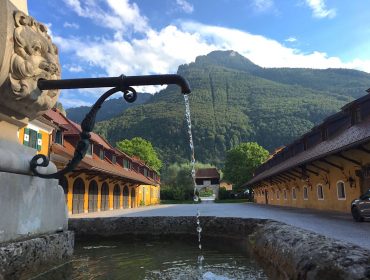 Löwenkopf-Wasserreiter-Brunnen, Innenhof, Gebäude und grüner Berg unter einem blauen Himmel.