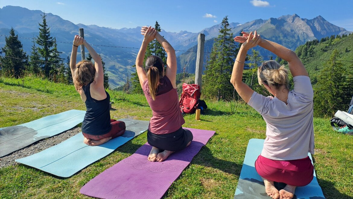 © Rauriser Hochalmbahnen Drei Frauen machen draußen auf Matten Yoga, umgeben von Bergen und Bäumen unter blauem Himmel. (vergrößerte Ansicht)