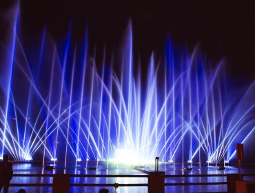 Leuchtend blaue und weiße Fontänen beleuchten den Zellersee bei Nacht und erzeugen dramatische Muster auf dem Wasser.