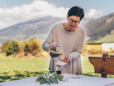 Eine Frau gießt Flüssigkeit durch ein Filterpapier im Freien mit Bergen im Hintergrund.