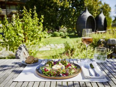 Ein Teller mit Salat, Brot und Roséwein für den perfekten Biogenießer-Moment in einem sonnigen Garten.