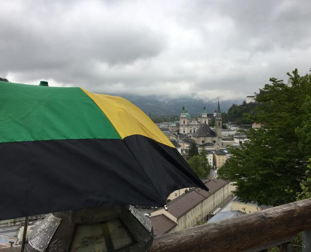 Hinter einem aufgespannten Regenschirm sieht man die Altstadt Salzburgs im dichten Regen.