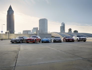 Sechs Porsche sind auf einem Dach aufgereiht, mit modernen Stadtgebäuden im Hintergrund.