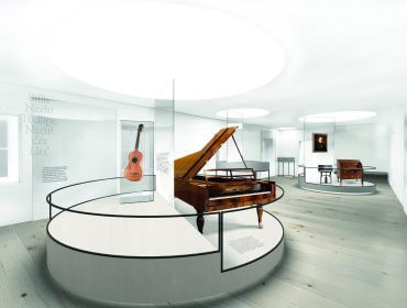 Moderner Museumsraum mit einem Flügel, einer Gitarre und anderen Musikinstrumenten, die in Vitrinen ausgestellt sind.