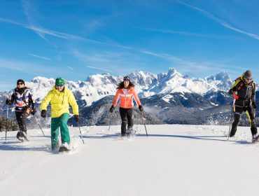 Tennengau Schneeschuhwandere © bernhardrmoser (1) Vier Personen beim Schneeschuhwandern auf frischem Schnee mit verschneiten Bergen und blauem Himmel im Hintergrund.