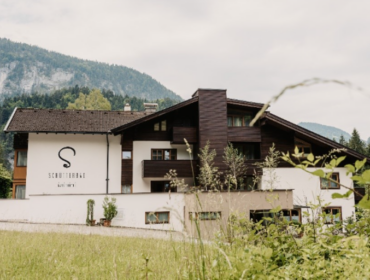 Moderne Almhütte mit dunklen Holzakzenten, umgeben von Grün und Bergen im Hintergrund.