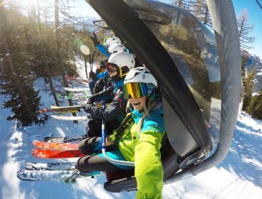 Elisa Deutschmann Altenmarkt-Zauchensee-10 Eine Gruppe von Skifahrern in farbenfroher Kleidung fährt mit einem Skilift - perfekte myinstaweekend-Vibes auf verschneiten Pisten und in der Sonne liegenden Bäumen.