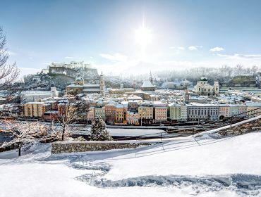 Blick vom Kapuzinerberg auf die Altstadt mit Festung Hohensalzburg Verschneites Stadtbild mit bunten Gebäuden, Bäumen und einer Entdeckerfestung im Salzburger Land in der Wintersonne.