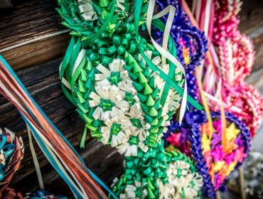 Bunte handgemachte Strohkränze mit Bändern präsentieren charmantes Handwerk an einer Holzwand.