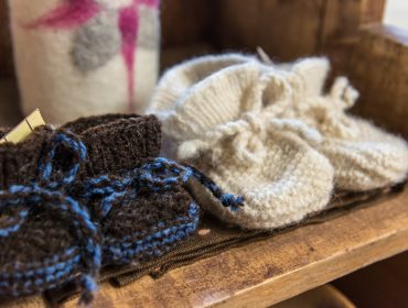 Wollstadl – Stricken Zwei Paar gestrickte Babyschühchen, handgemachtes Handwerk in Braun und Weiß, ausgestellt auf einer Holzfläche.