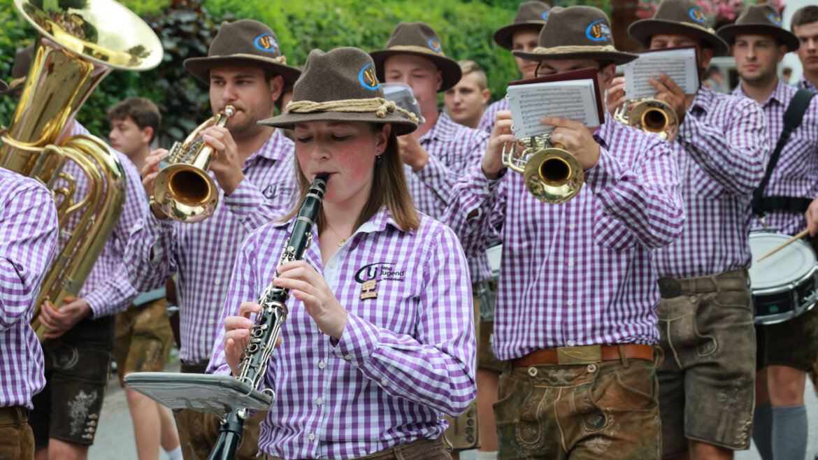 Ein Spielmannszug in karierten Hemden und Hüten spielt bei einer Parade im Freien. (vergrößerte Ansicht)