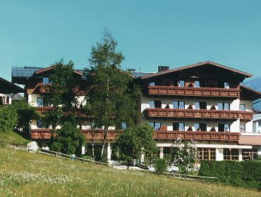 Ein großes Gebäude im alpinen Stil mit Holzbalkonen, umgeben von Bäumen und einer Wiese unter freiem Himmel.