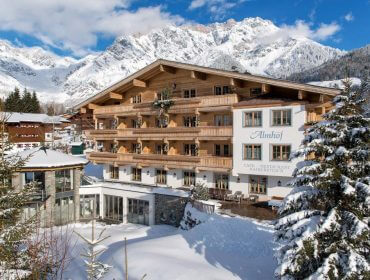 Ein Alpenhotel aus Holz, umgeben von schneebedeckten Bäumen und Bergen unter einem strahlend blauen Himmel.