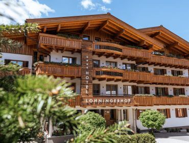 Hölzernes Alpenhotel mit Balkonen, Blumenkästen und Lohningerhof-Schild, unter blauem Himmel.