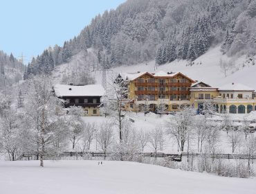 Gebäude inmitten von schneebedeckten Bäumen und Hügeln unter einem klaren blauen Himmel in einer Winterlandschaft.