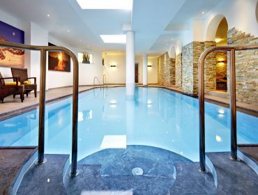 Modernes Hallenbad mit Steinwänden, Liegestühlen und heller Deckenbeleuchtung.