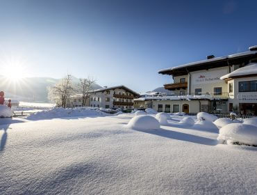 Ein schneebedecktes Hotel im Sonnenlicht, umgeben von Bergen und einer winterlichen Landschaft.