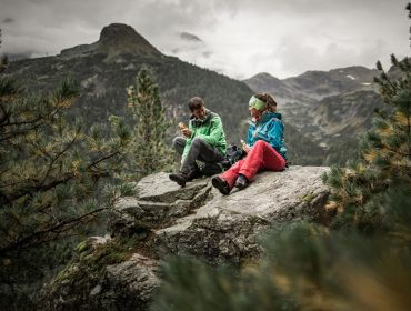 Zwei Personen in Wanderkleidung genießen eine Mahlzeit auf einem Felsen, während sie die Walderlebnisse Uttendorfs in den Zirbenwäldern und auf den Bergen auf sich wirken lassen.