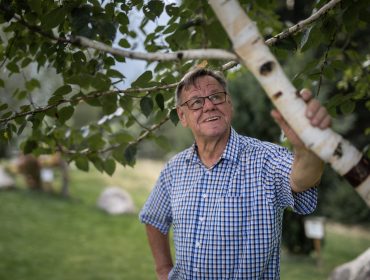 Älterer Mann im blau-karierten Hemd genießt walderlebnisse uttendorf, lächelnd mit Grünzeug hinter ihm.