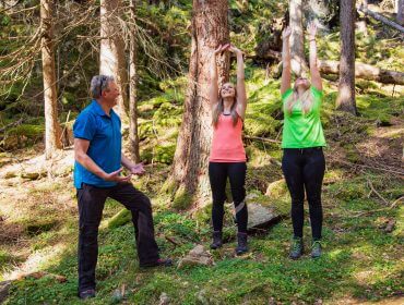 Drei Menschen stehen in einem Salzburger Lungauer Wald, zwei recken sich in die Höhe, einer gestikuliert und beobachtet.
