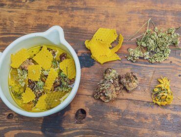 Eine weiße Schale mit Öl, Kräutern und Bienenwachs erinnert an Walderlebnis Saalachtal auf einem rustikalen Holztisch.