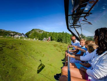 Die Familie fährt mit der Gamskogelbahn über grüne Hügel und Berge und genießt die sonnige Aussicht.