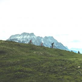 Familie mit dem Mountainbike im Gegenlicht, im Hintergrund Bergkulisse