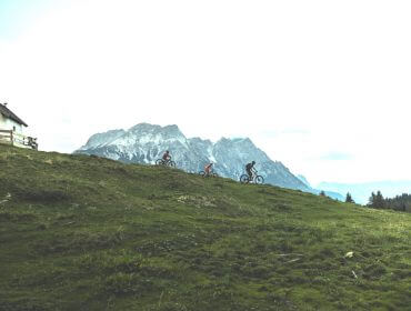 Familie mit dem Mountainbike im Gegenlicht, im Hintergrund Bergkulisse