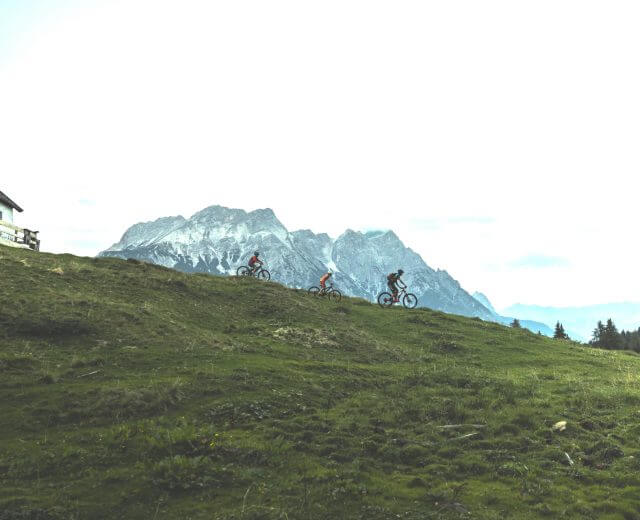 Familie mit dem Mountainbike im Gegenlicht, im Hintergrund Bergkulisse