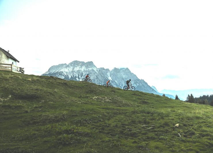 Familie mit dem Mountainbike im Gegenlicht, im Hintergrund Bergkulisse
